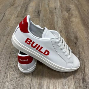 a pair of white sneakers with red heel and company logo on sides, placed on a wooden floor