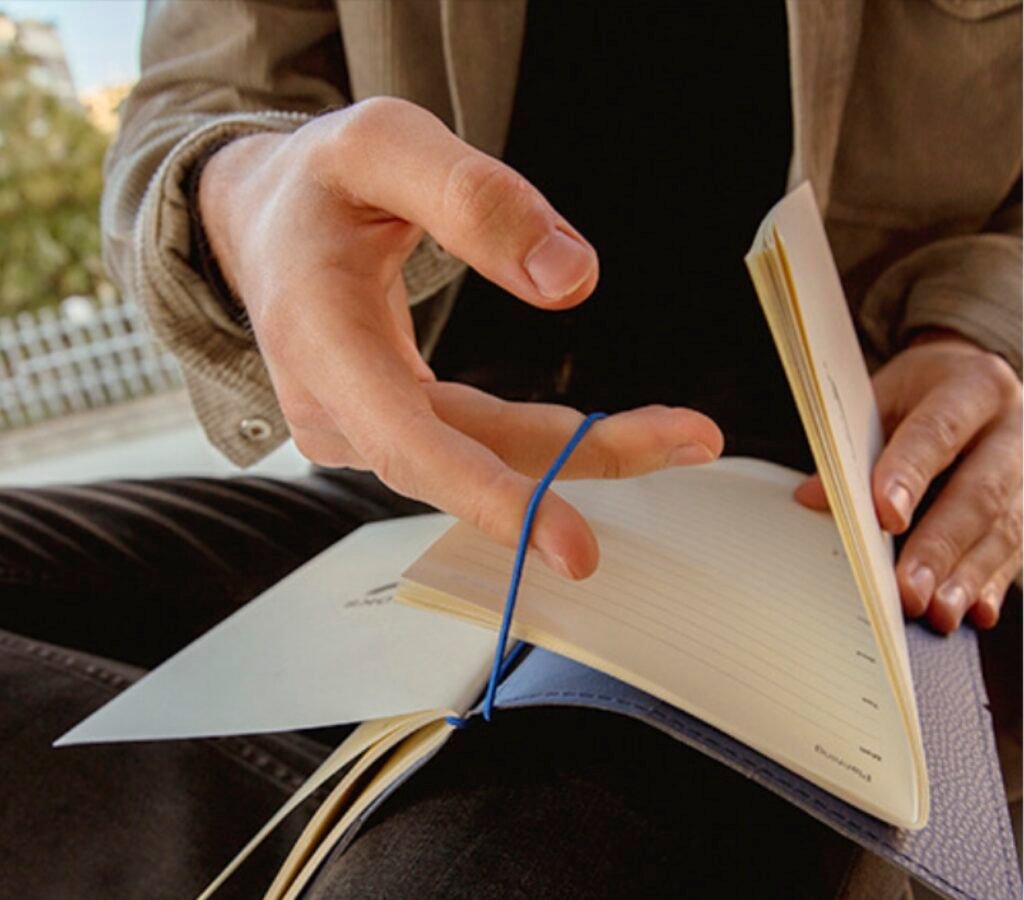 A man holding in hand a bullet journal open inserting 1 jorunal